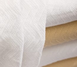 A stack of herringbone blankets in white and champagne are lightweight blankets.