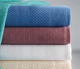 WIth a woven block pattern, the Snagless Hospital Blanket is shown here in a stack of 5 colors Blue, Cream, Rose, Teal, & White.