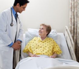 Doctor speaking with female patient wearing a Risk Identity Patient Gown. This hospital gown is a lapover V-neck style made from Champion Cloth fabric, with I.V. sleeves and telemetry pockets in Kaleidoscope Yellow color.