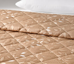 The Mary Jane Quilted bedspread shown here on a bed, features a leaf pattern on an Almond background.