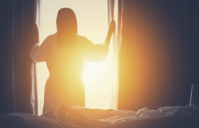 Woman standing in front of a window opening curtains
